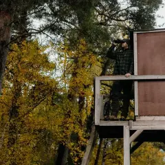 Myśliwy w ambonie, wypatrujący zwierzyny płowej w nocy. Jesienne liście drzew tworzą tło.