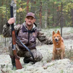 Myśliwy w kamuflażu z psem i strzelbą, gotowi do polowania. Różne sposoby polowania wymagają odpowiedniego przygotowania.