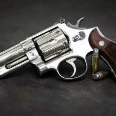 Błyszczący rewolwer .357 Magnum z drewnianą rękojeścią i dwoma nabojami obok. Jeden z wielu rodzajów broni palnej.