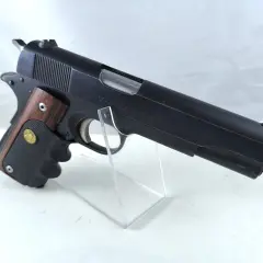 Klasyczny pistolet Colt Government Model kaliber 45, z drewnianą okładziną rękojeści, prezentowany na przezroczystym stojaku.