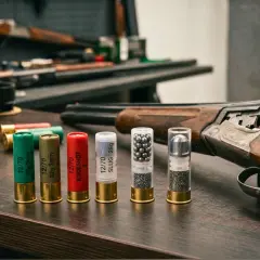 Na stole leżą naboje, w tym jeden z napisem BUCKSHOT, obok strzelby i pudełka z amunicją.