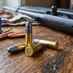 Kilka naboi kalibru .22 LR leży na drewnianym stole obok karabinu Ruger. To przygotowanie do elaboracji amunicji.