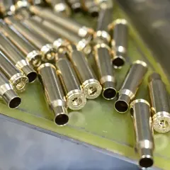 Złote łuski nabojów leżą w metalowej tacce, gotowe do dalszej produkcji amunicji.
