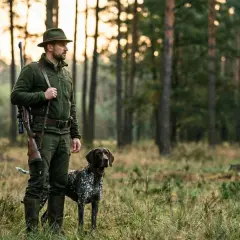 Myśliwy w leśnej scenerii z psem i bronią, jakby z vademecum myśliwego.