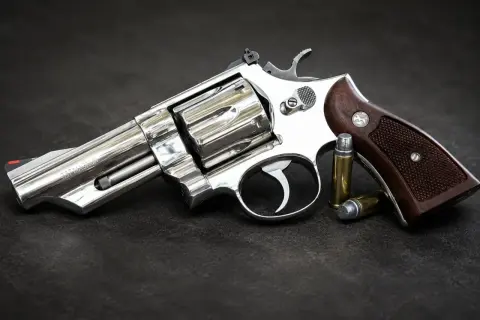 Błyszczący rewolwer .357 Magnum z drewnianą rękojeścią i dwoma nabojami obok. Jeden z wielu rodzajów broni palnej.