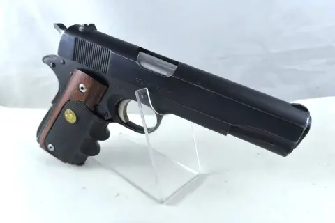 Klasyczny pistolet Colt Government Model kaliber 45, z drewnianą okładziną rękojeści, prezentowany na przezroczystym stojaku.