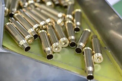 Złote łuski nabojów leżą w metalowej tacce, gotowe do dalszej produkcji amunicji.