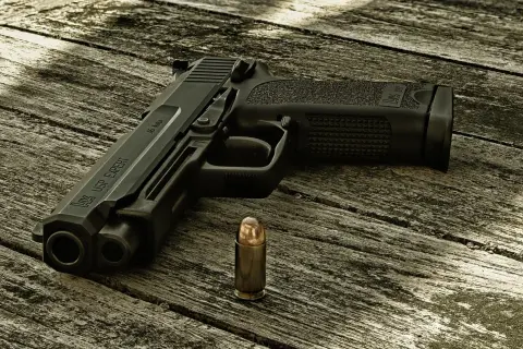 Pistolet HK USP EXPERT kaliber .45 Auto i nabój na drewnianym stole.