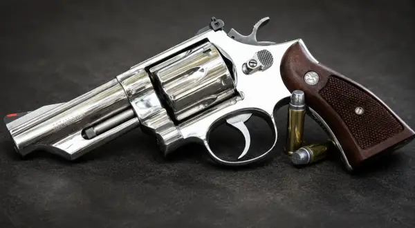 Błyszczący rewolwer .357 Magnum z drewnianą rękojeścią i dwoma nabojami obok. Jeden z wielu rodzajów broni palnej.
