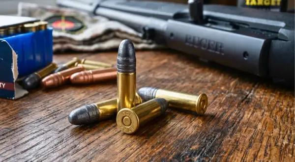 Kilka naboi kalibru .22 LR leży na drewnianym stole obok karabinu Ruger. To przygotowanie do elaboracji amunicji.