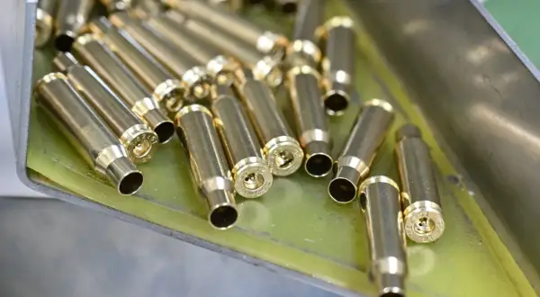 Złote łuski nabojów leżą w metalowej tacce, gotowe do dalszej produkcji amunicji.