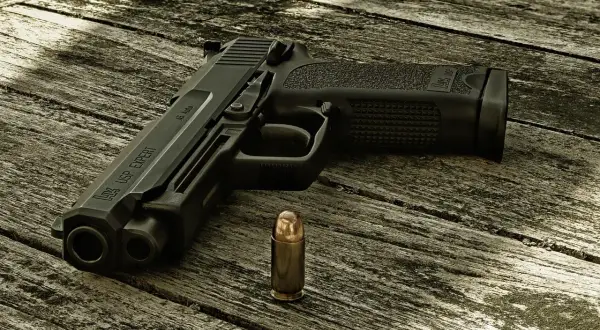 Pistolet HK USP EXPERT kaliber .45 Auto i nabój na drewnianym stole.