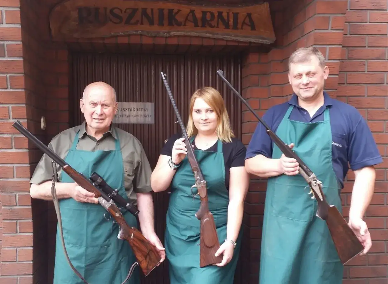Trzech pracowników zakładu rusznikarskiego pozuje z bronią.