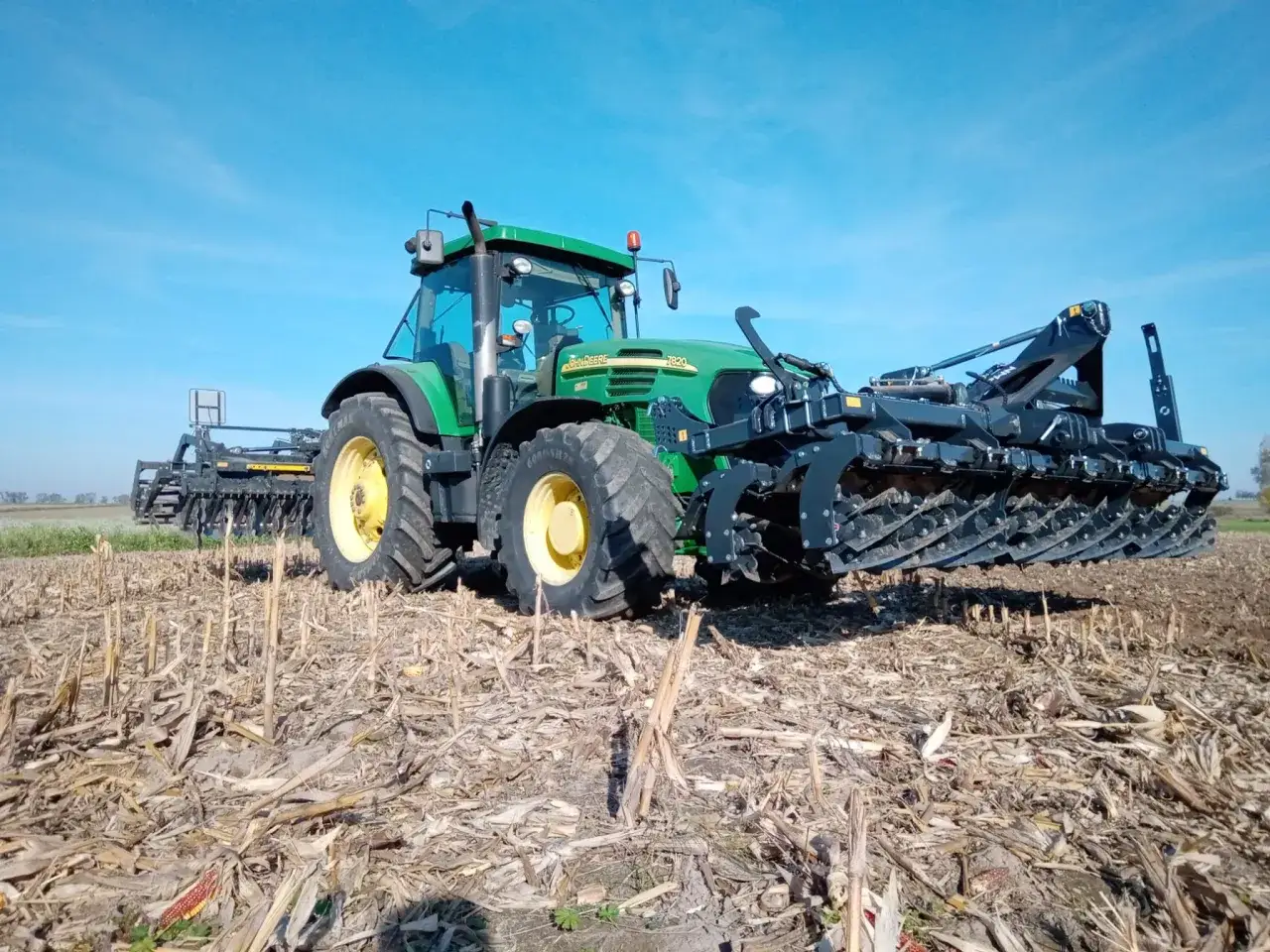 Zielony traktor John Deere z agregatem uprawowym przygotowuje poletka łowieckie do siewu.