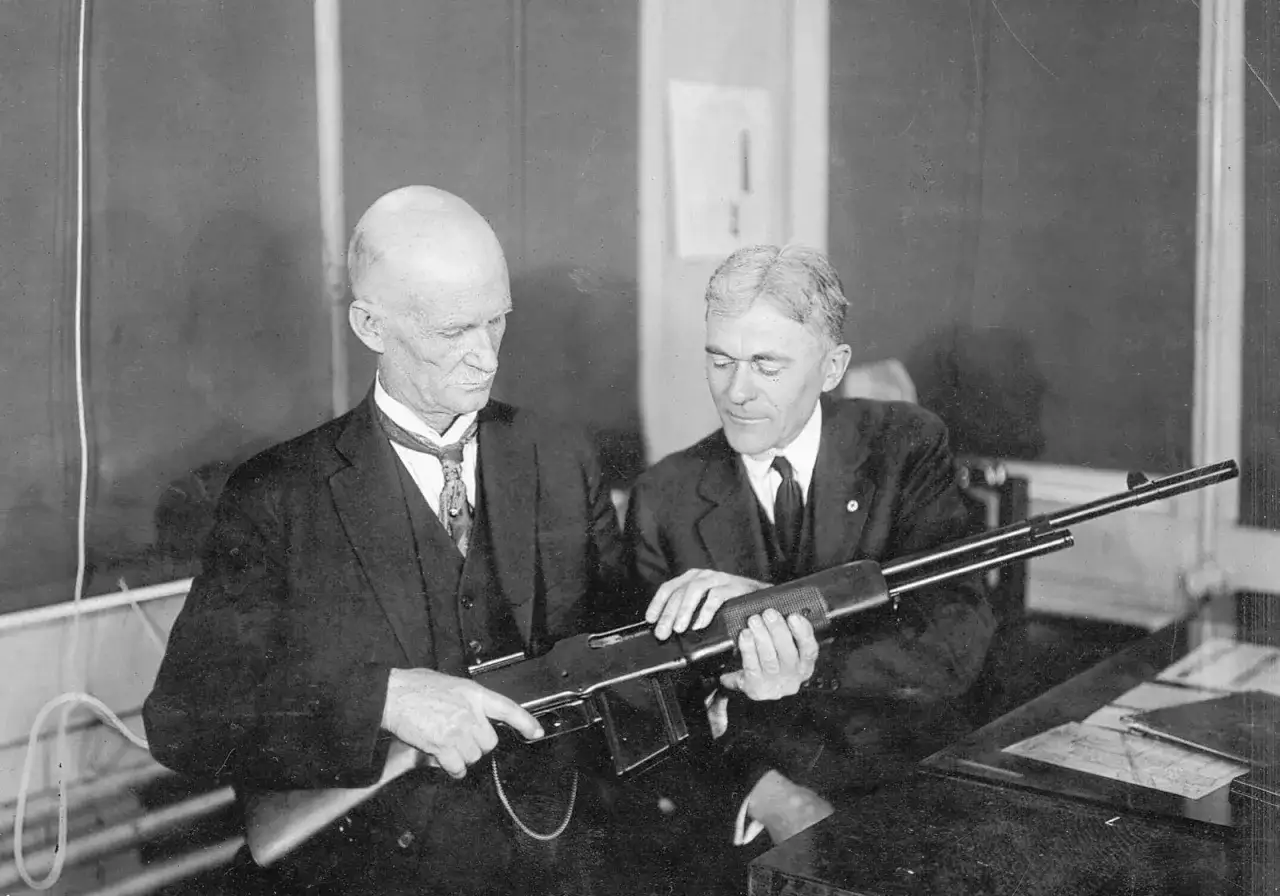 Dwóch mężczyzn ogląda karabin. Jeden z nich, z łysą głową, to prawdopodobnie sam John Browning, legendarny konstruktor broni.