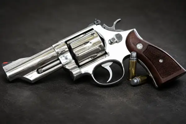 Błyszczący rewolwer .357 Magnum z drewnianą rękojeścią i dwoma nabojami obok. Jeden z wielu rodzajów broni palnej.