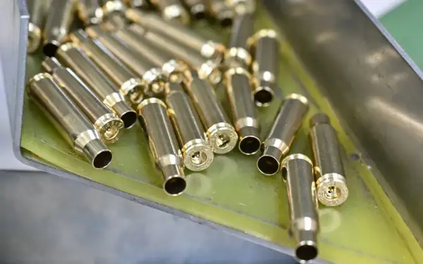 Złote łuski nabojów leżą w metalowej tacce, gotowe do dalszej produkcji amunicji.